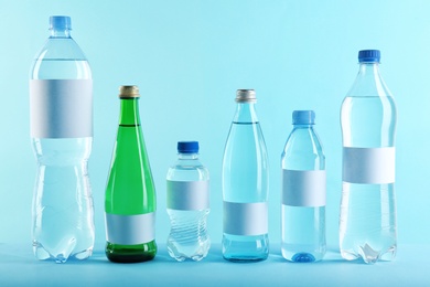 Different bottles of pure water with blank tags on color background