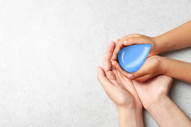 Image of Woman and her child holding water drop on grey stone background, top view with space for text. Ecology protection