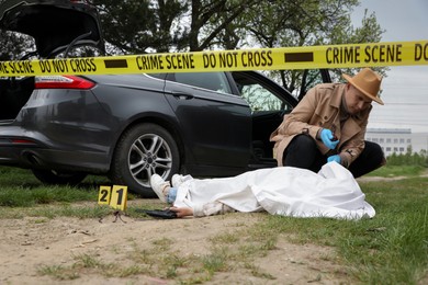 Photo of Investigator working at crime scene with dead body outdoors