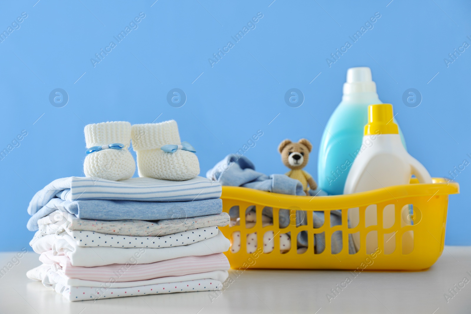 Photo of Detergents and children's clothes on white table near blue wall