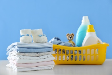 Photo of Detergents and children's clothes on white table near blue wall