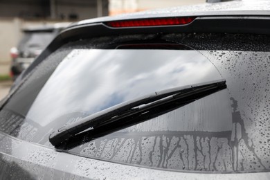 Car wiper cleaning water drops from rear windshield glass outdoors, closeup