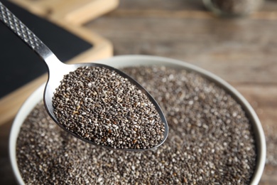 Photo of Closeup of spoon with chia seeds over bowl on blurred background