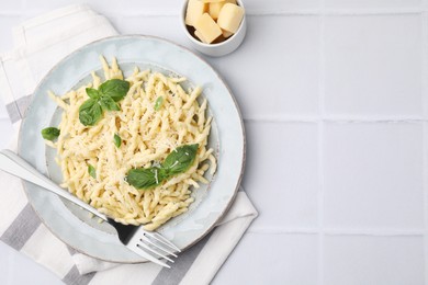 Plate of delicious trofie pasta with cheese, basil leaves and fork on white tiled table, flat lay. Space for text