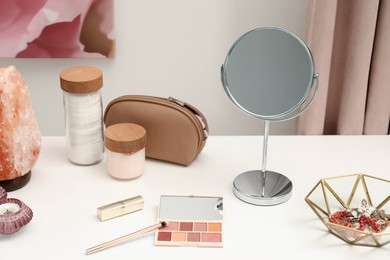 Photo of Dressing table with mirror, cosmetic products, jewelry and burning candle in makeup room
