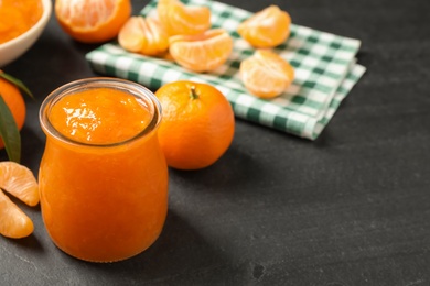 Tasty tangerine jam in glass jar on dark table, space for text