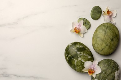 Flat lay composition with spa stones and orchid flowers on white marble table. Space for text