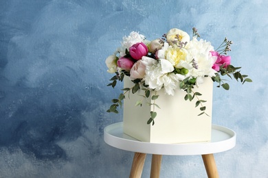 Photo of Box with bouquet of beautiful flowers on table against color background