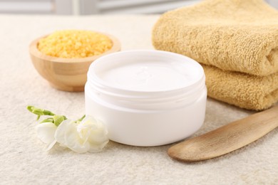 Photo of Body care. Moisturizing cream in open jar and flower on light textured table, closeup