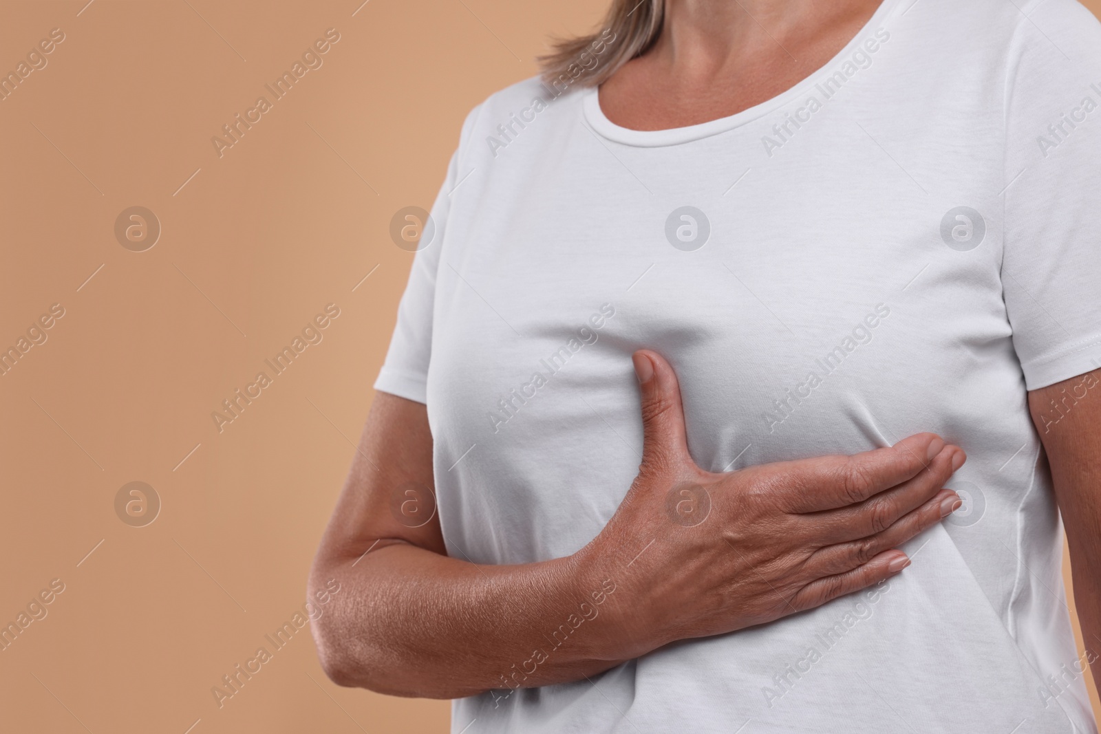 Photo of Woman doing breast self-examination on light brown background, closeup. Space for text