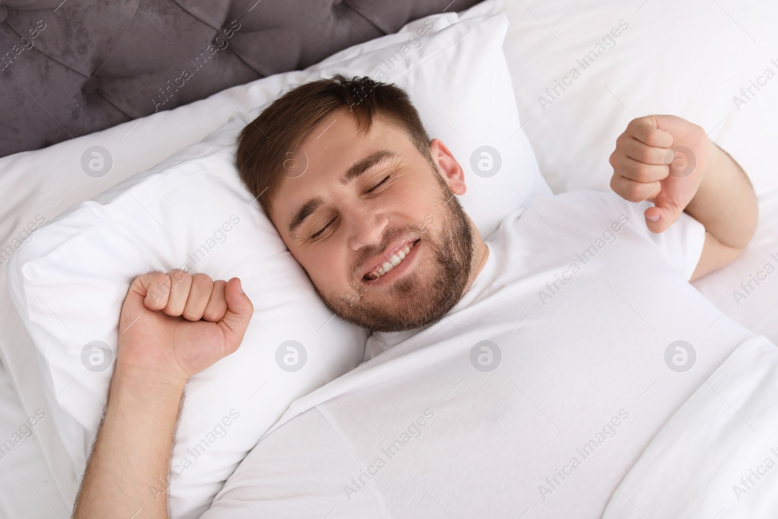 Photo of Young happy man waking up after sleeping in bed at home. Early morning