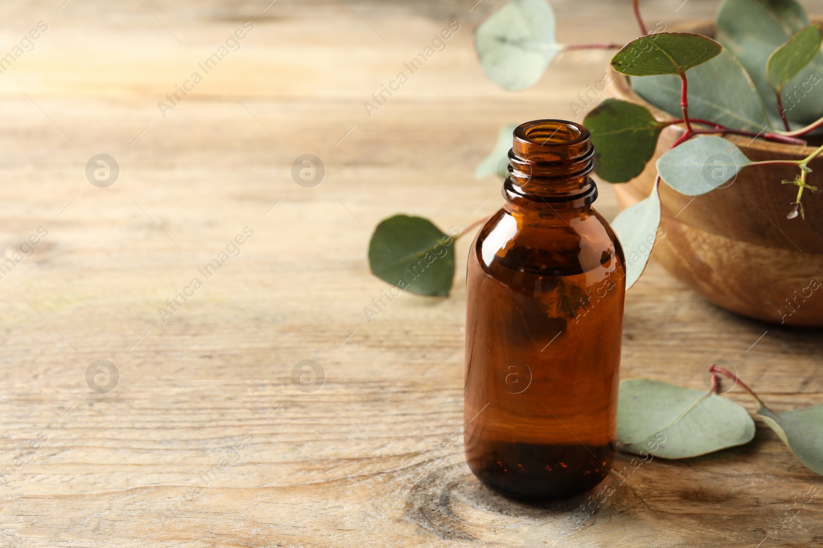 Photo of Bottle of eucalyptus essential oil and leaves on wooden table. Space for text