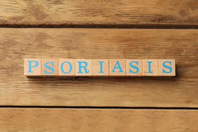Photo of Word Psoriasis made of cubes with letters on wooden table, top view