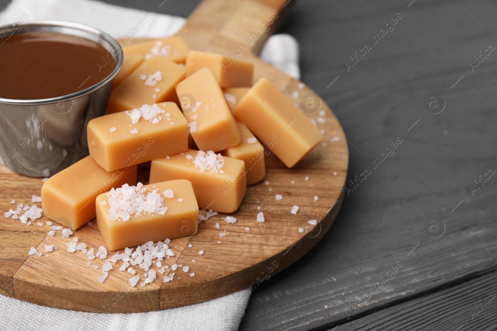 Photo of Yummy caramel candies and sea salt on wooden table, closeup. Space for text