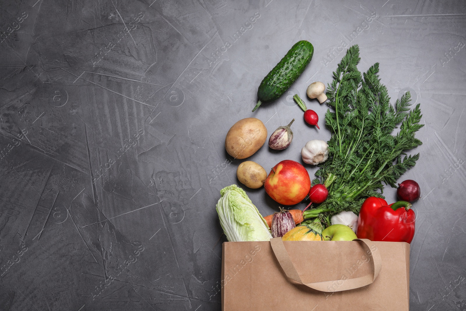 Photo of Paper bag with fresh vegetables and apples on dark background, flat lay. Space for text