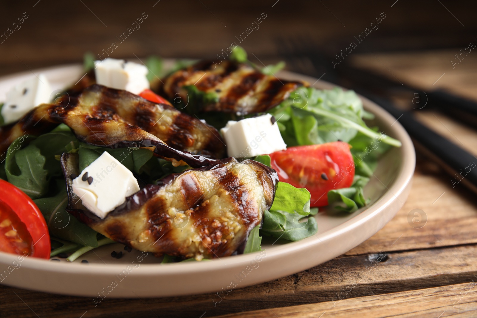 Photo of Delicious salad with roasted eggplant, feta cheese and arugula served on wooden table, closeup