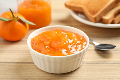 Photo of Tasty tangerine jam in bowl on wooden table