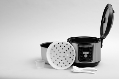 Photo of Modern electric multi cooker, parts and accessories on grey background. Space for text