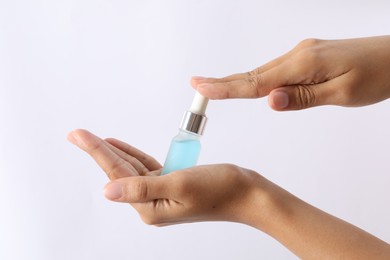 Photo of Woman with bottle of cosmetic serum on white background, closeup