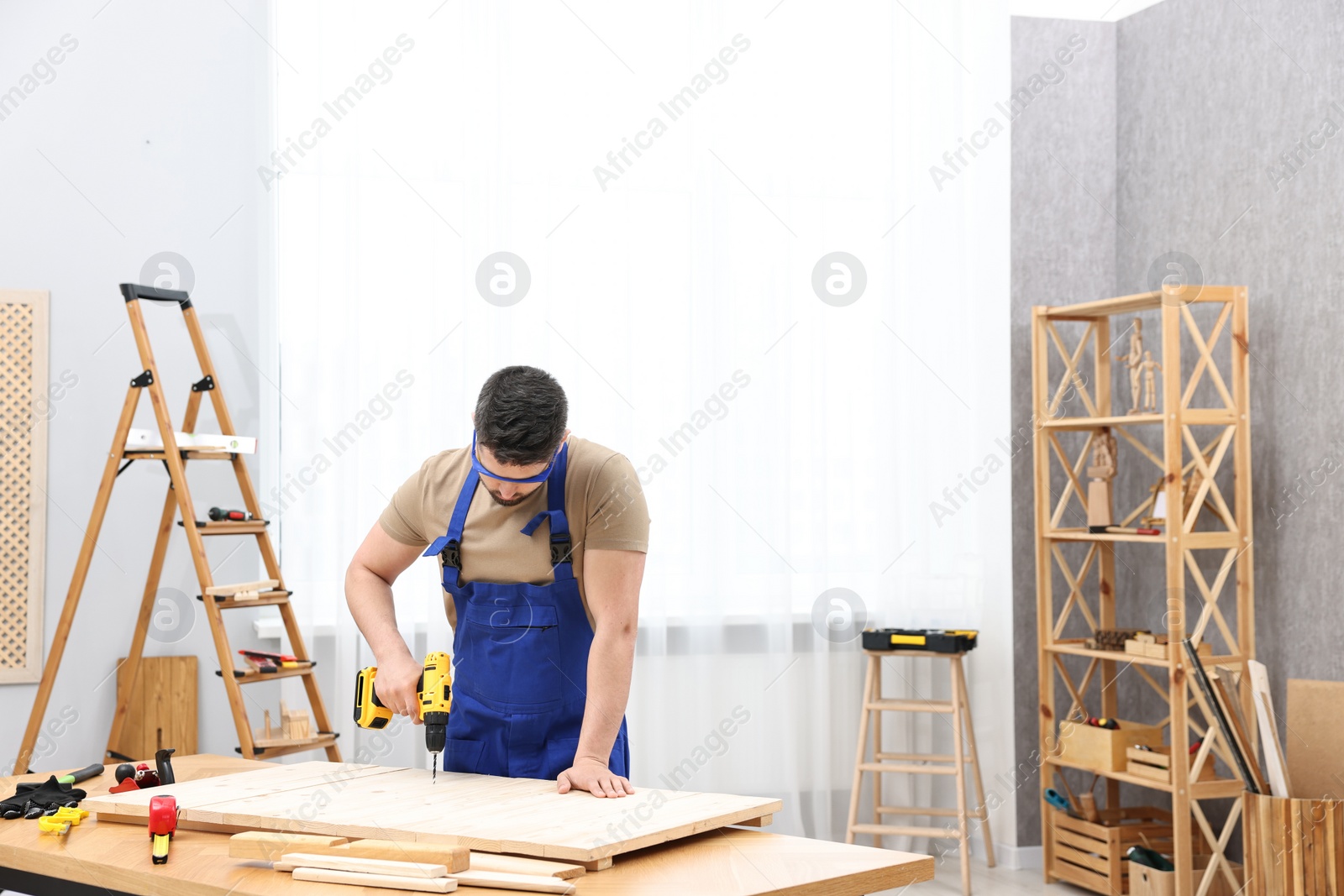 Photo of Young worker using electric drill at table in workshop