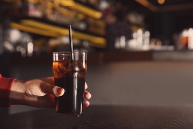 Man holding glass of refreshing cola at table indoors, closeup. Space for text