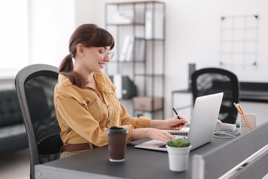 Woman taking notes during webinar at table indoors