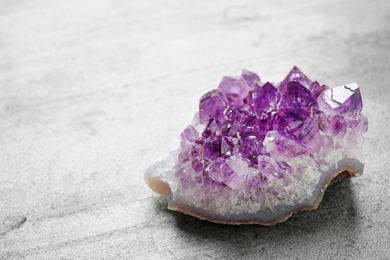 Photo of Beautiful purple amethyst gemstone on grey table, space for text