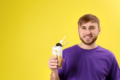 Young man with glass of delicious milk shake on color background