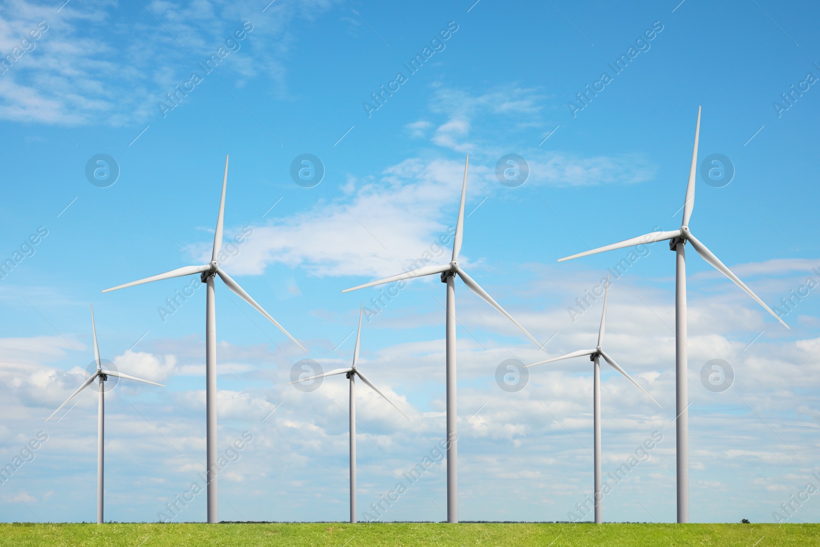 Image of Alternative energy source. Wind turbines in field under blue sky