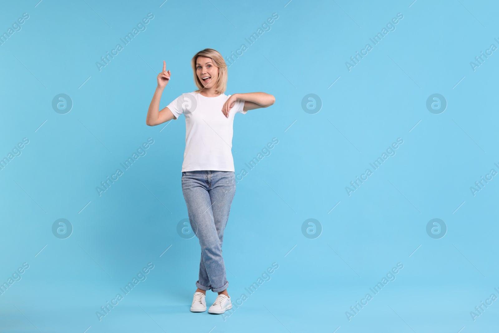 Photo of Happy woman pointing on light blue background, space for text
