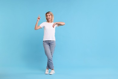 Happy woman pointing on light blue background, space for text