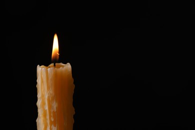 Photo of Burning church wax candle on black background, space for text
