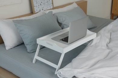 White tray table with laptop on bed indoors