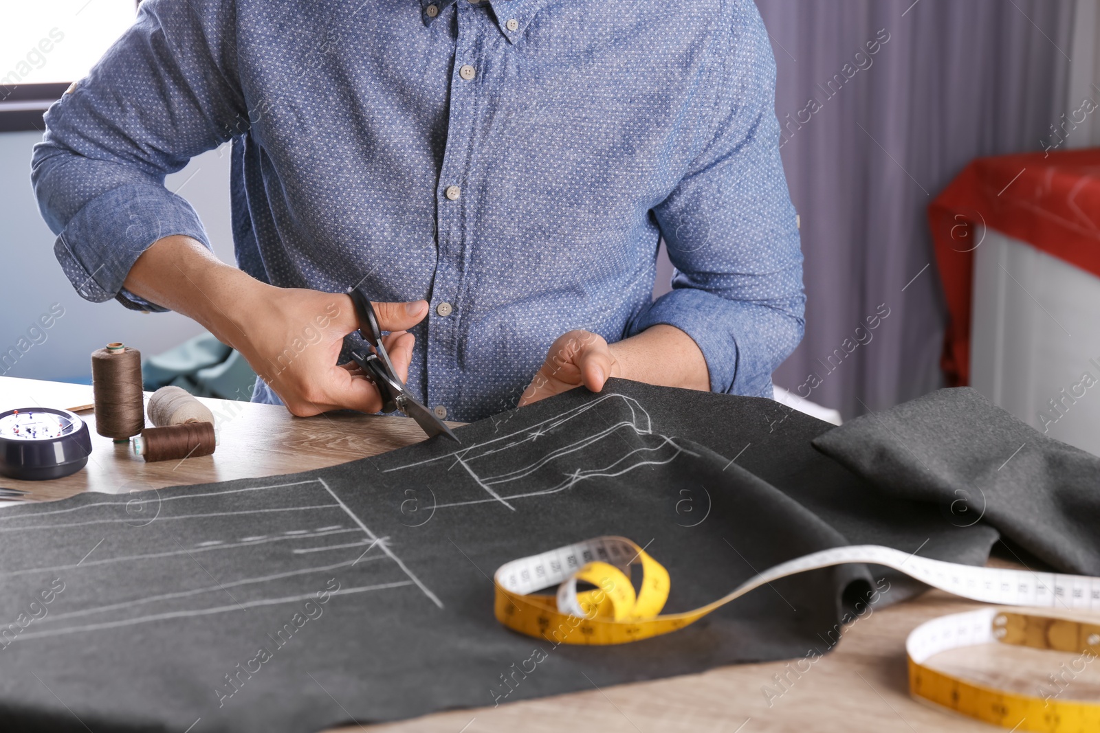 Photo of Tailor cutting fabric at table in atelier, closeup