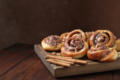 Photo of Tasty cinnamon rolls, sticks and nuts on wooden table, space for text