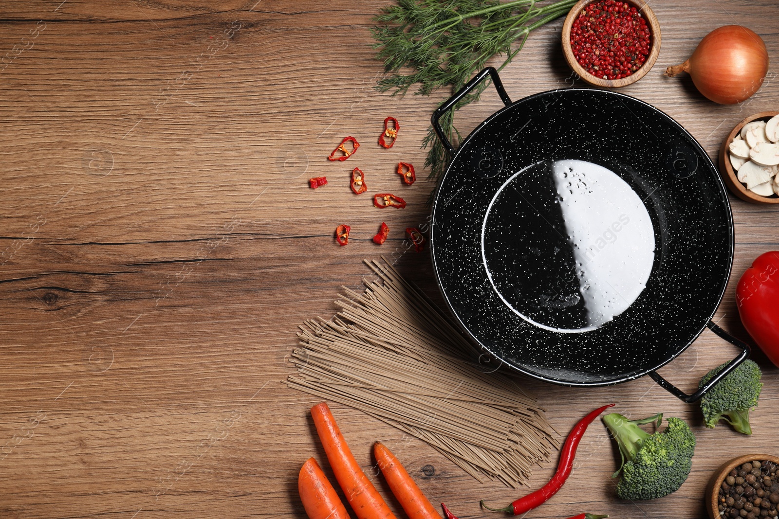 Photo of Empty iron wok surrounded by raw ingredients on wooden table, flat lay. Space for text