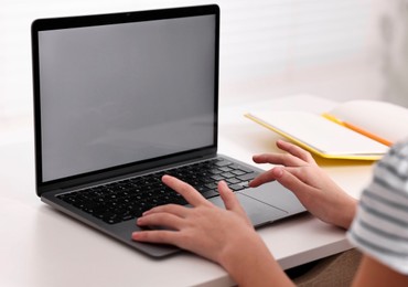 E-learning. Girl using laptop during online lesson at table indoors, closeup