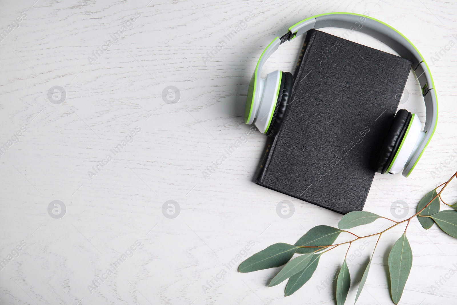 Photo of Modern headphones with hardcover book on white wooden background, top view. Space for text