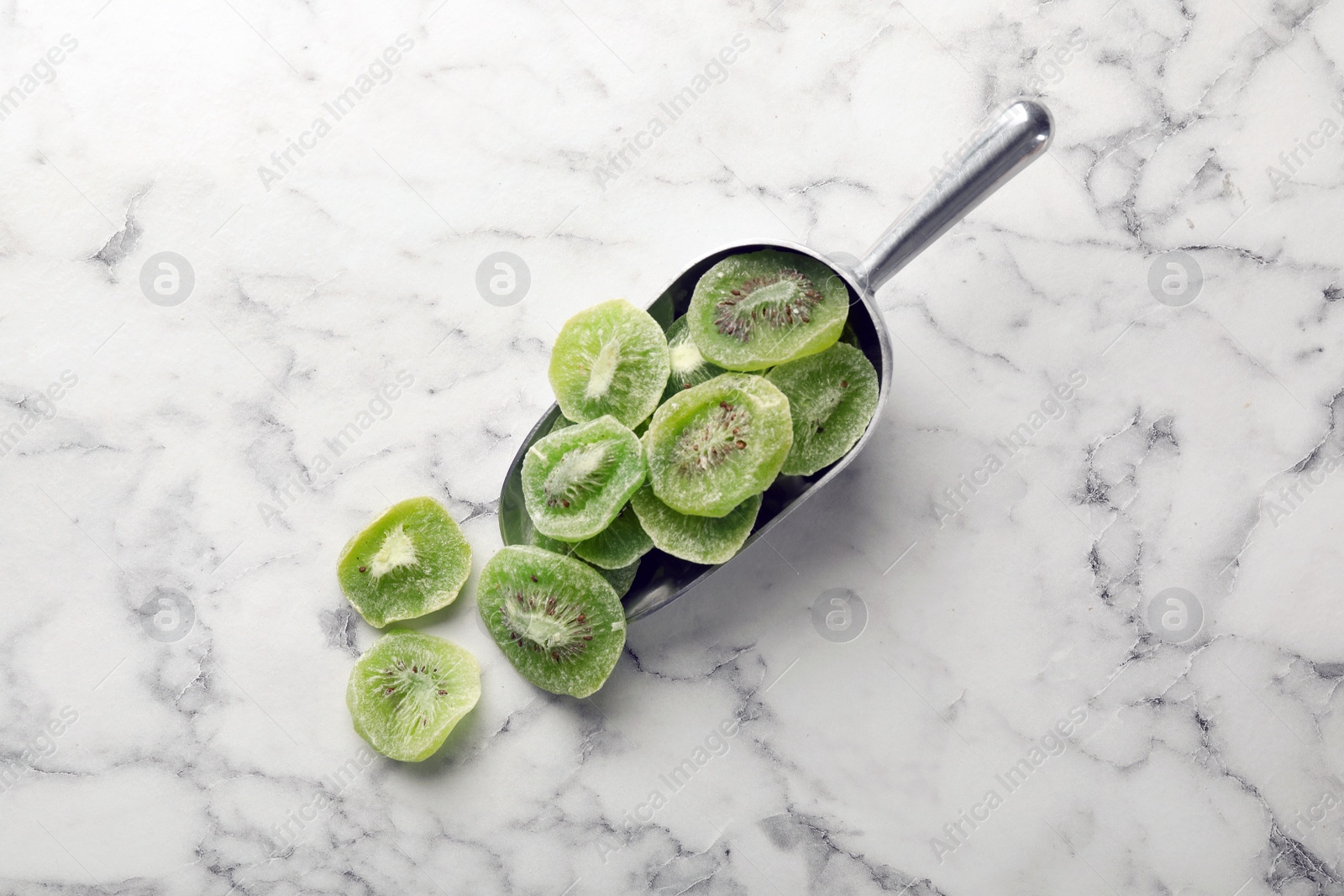 Photo of Scoop with slices of kiwi on marble background, top view. Dried fruit as healthy food