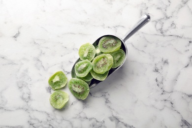 Photo of Scoop with slices of kiwi on marble background, top view. Dried fruit as healthy food