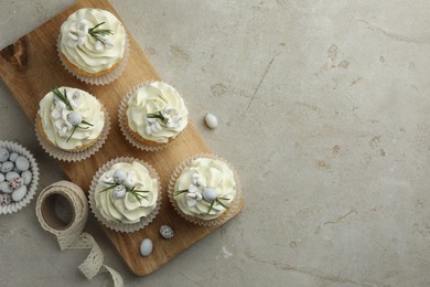 Tasty Easter cupcakes with vanilla cream, candies and ribbon on gray table, flat lay. Space for text