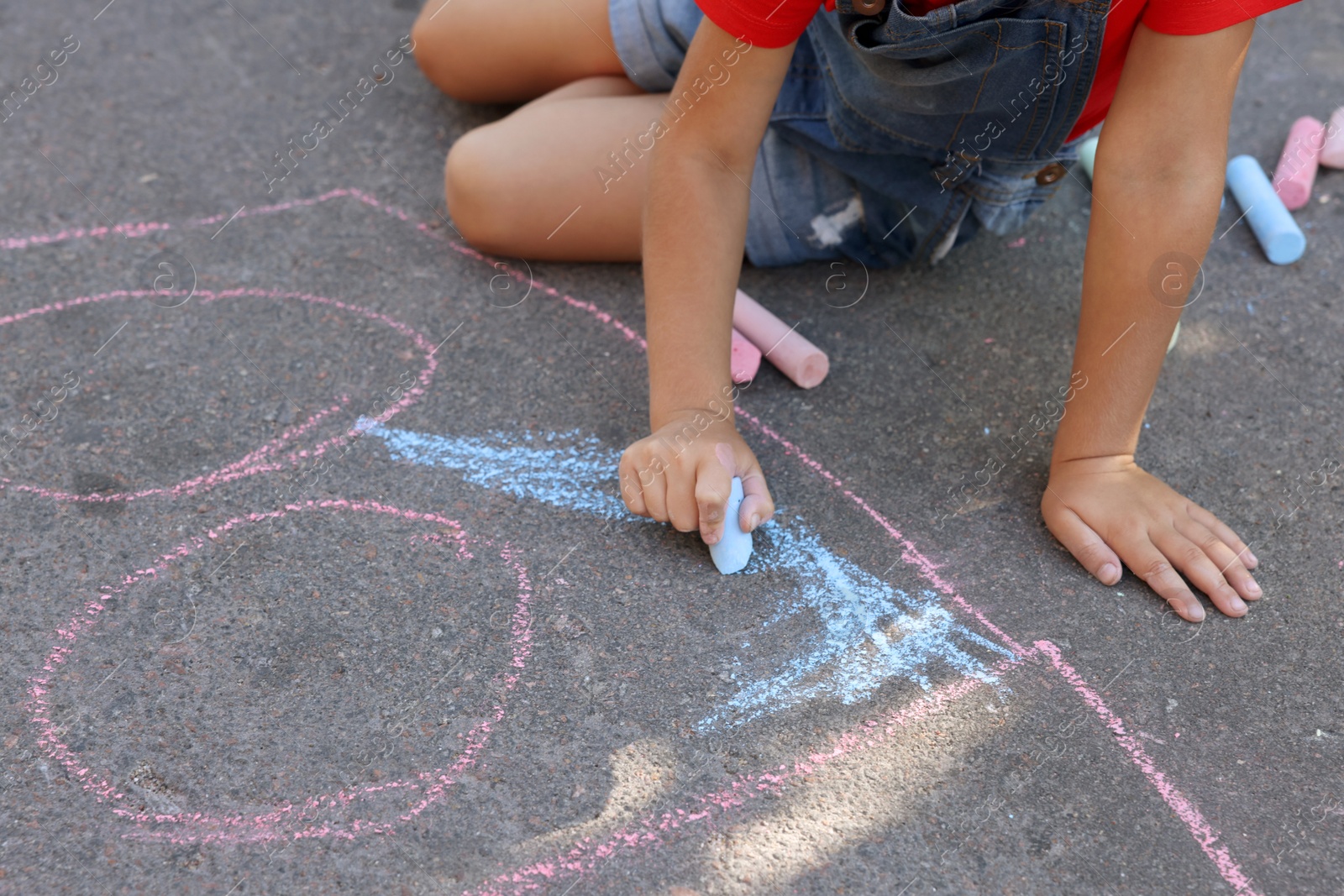 Photo of Little child drawing with colorful chalk on asphalt, closeup