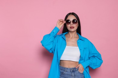 Photo of Attractive serious woman touching fashionable sunglasses against pink background. Space for text