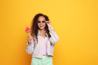 Photo of Beautiful young African American woman with piece of watermelon on yellow background. Space for text