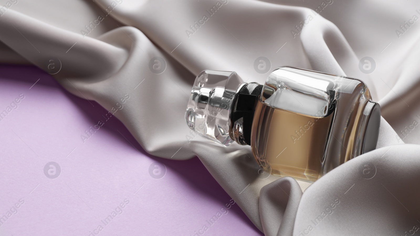 Photo of Luxurious bottle of perfume and beige silk on pink background, closeup. Space for text