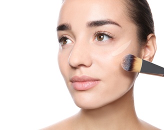 Photo of Young woman applying foundation on her face against white background