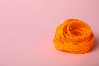 Photo of Orange shoe lace on light pink background. Space for text