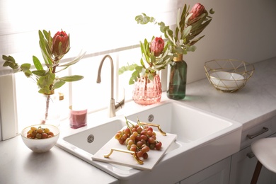 Vases with beautiful protea flowers near sink in kitchen. Interior design