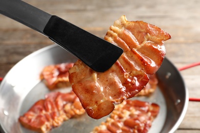 Photo of Tongs with fried bacon over table, closeup