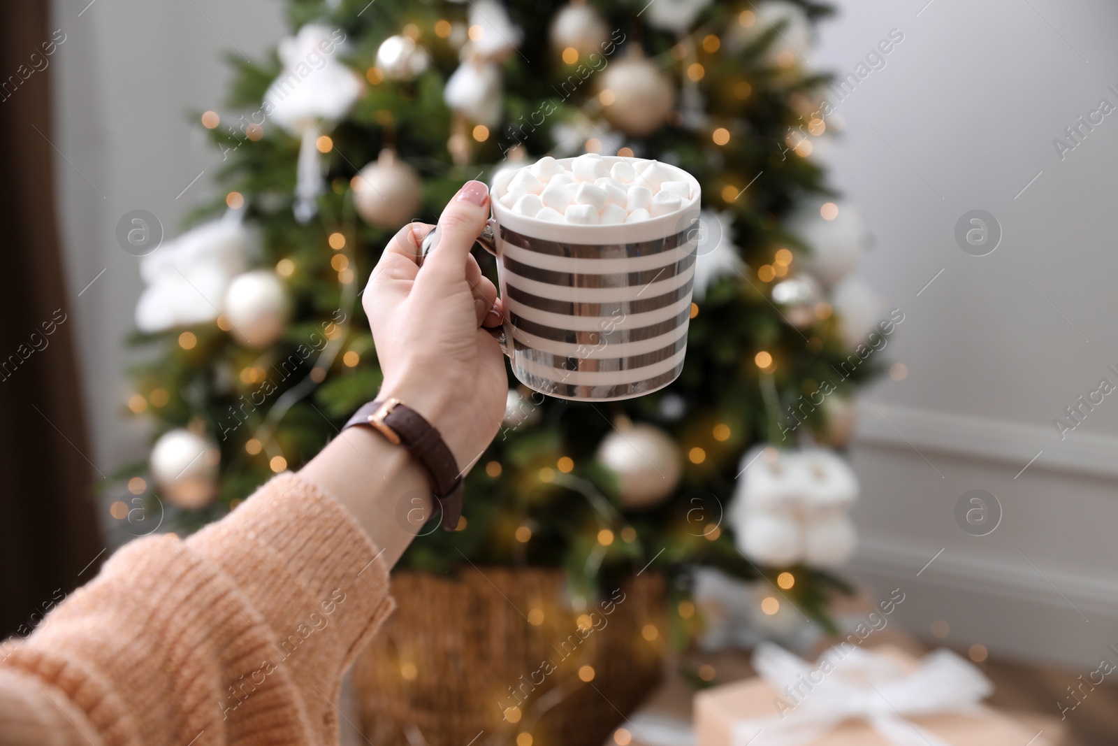 Photo of Woman with cup of delicious hot drink near Christmas tree at home, closeup